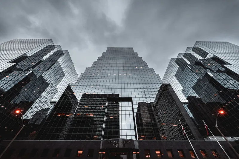 Three faceted glass skyscrapers seen from below under a heavy grey sky