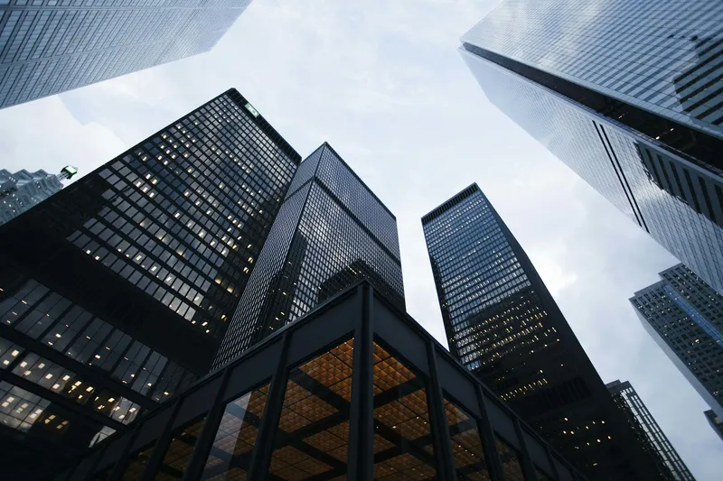 Looking straight up between dark glass towers into a pale sky