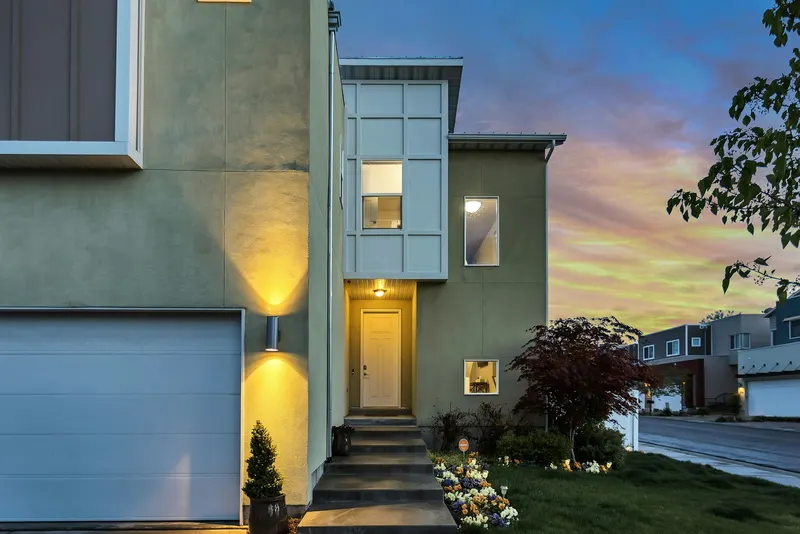 Green rendered house at sunset with warm wall lights beside the entrance steps
