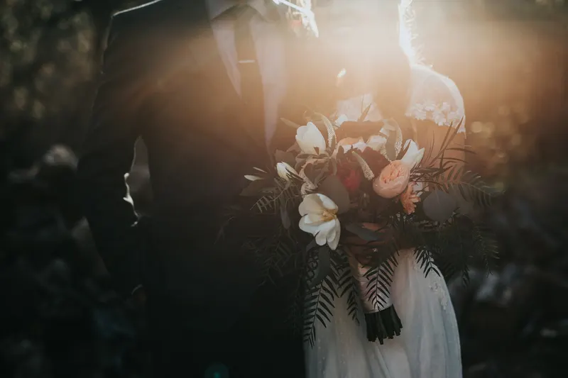 Backlit couple holding a bouquet of pale flowers in late golden light
