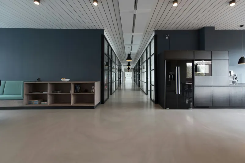 Long open-plan office interior with a grey kitchen and a corridor of ceiling lights